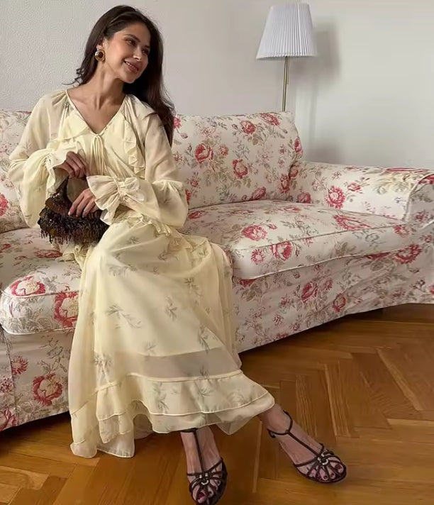 Frilly Maxi Dress - V-neck Ruffle A-line Dress in soft yellow with long sleeves, worn by a woman seated on a floral couch. Elegant autumn style.